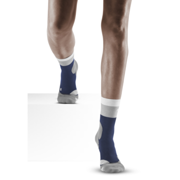 Lower legs of model walking in mid-cut CEP Hiking Light Merino compression socks in marine blue.