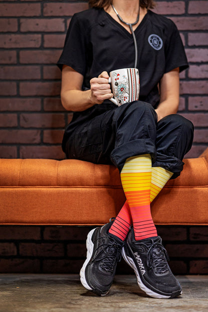 Medical professional wearing Lunatik Retro Renegade+ compression socks (rainbow stripes) with black sneakers.