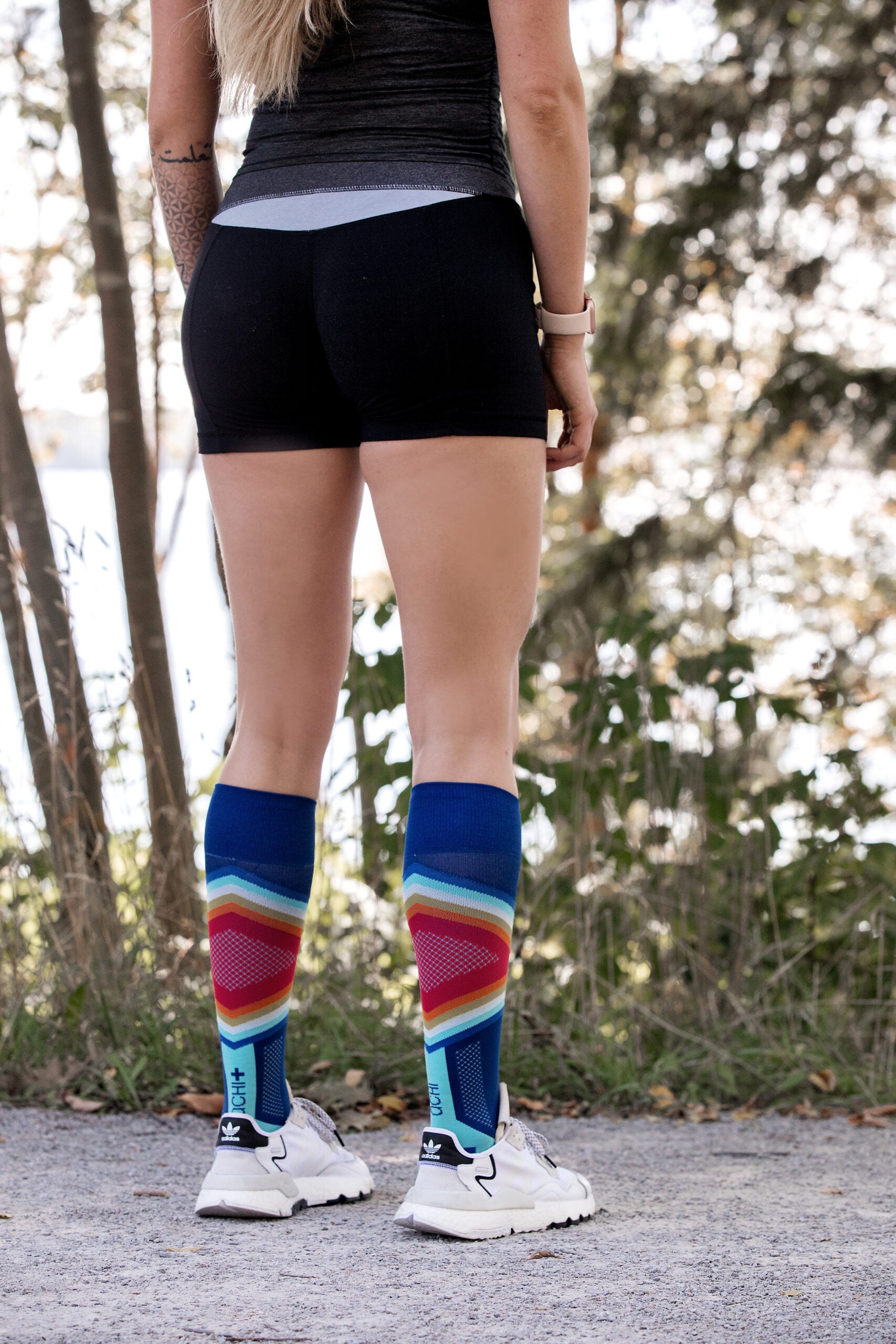 Lower body of a female model in Lunatik Propel Elite compression socks and white running shoes and sporty outfit.
