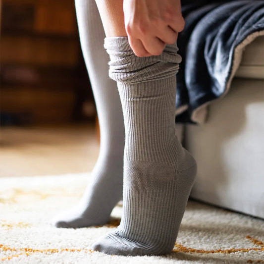 A woman in grey Bauerfeind merino compression socks standing on a rug.