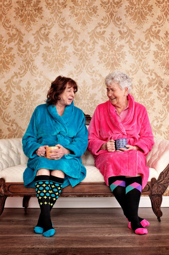 Two older women in bathrobes having tea together in Lunatik compression socks.